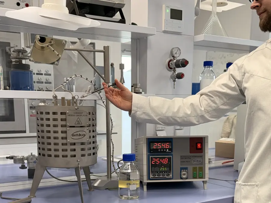 Eine Person in einem Laborkittel bedient in einem Labor einen beheizten Behälter aus Metall, während auf dem Labortisch eine digitale Steuereinheit und Flaschen stehen.