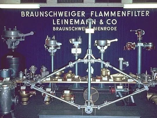 Display of various industrial flame arresters and safety devices mounted on stands in front of a Braunschweiger Flammenfilter exhibition backdrop.