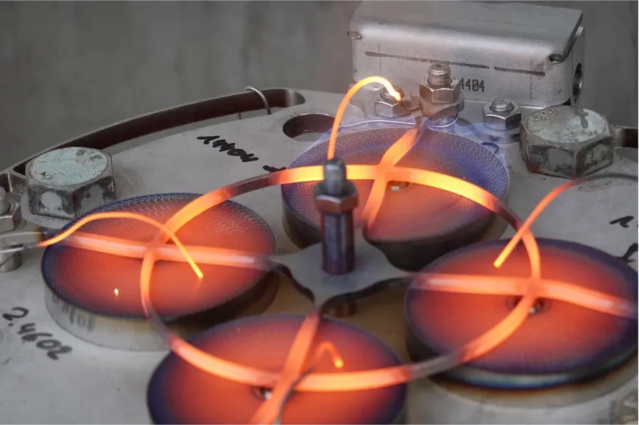Gros plan sur un appareil de test en laboratoire comportant des fils chauffés incandescents et des éléments métalliques circulaires, illustrant un montage expérimental actif à haute température.