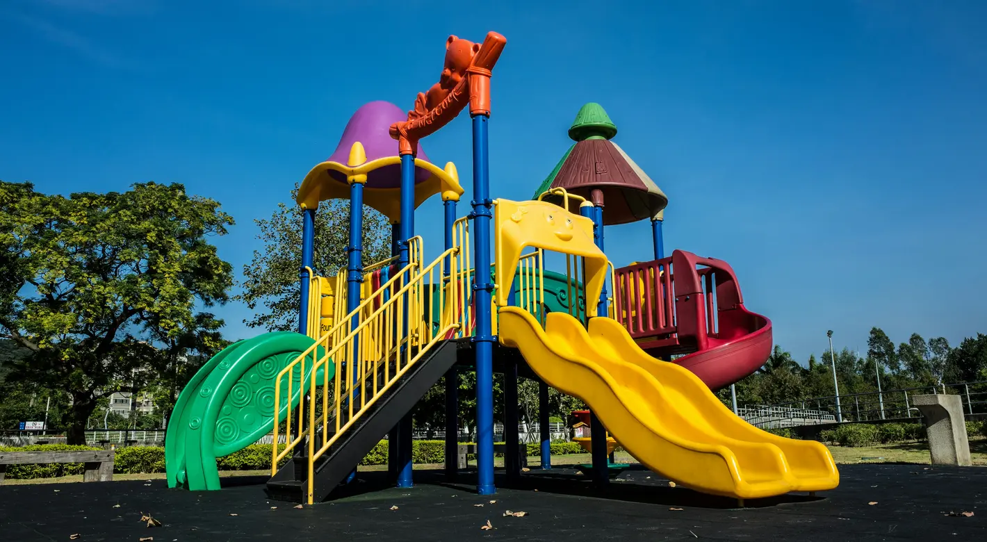 Unter strahlend blauem Himmel steht ein farbenfroher Spielplatz mit Rutschen und Kletterplattformen.