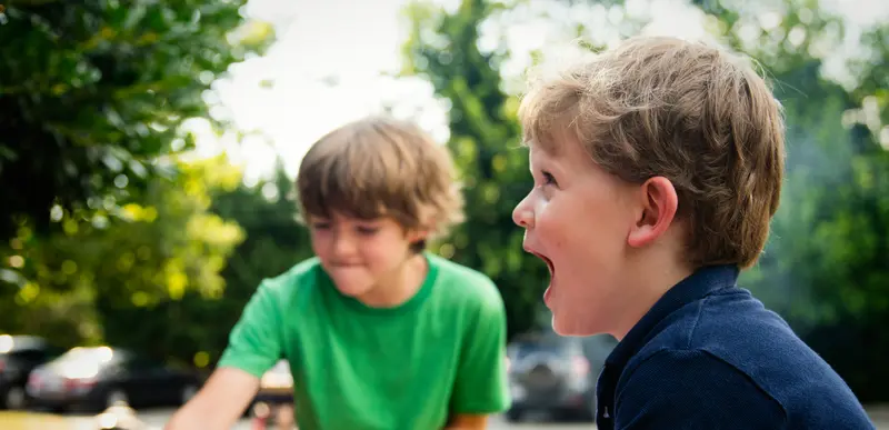 Two boys play at a small pink inflatable pool outdoors, with one boy laughing in the foreground.