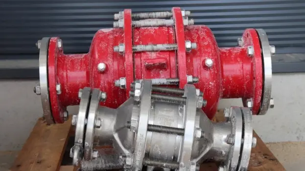 Two industrial inline safety devices or flame arresters, one red and one silver, resting on a wooden pallet with visible frost residue in an outdoor setting.