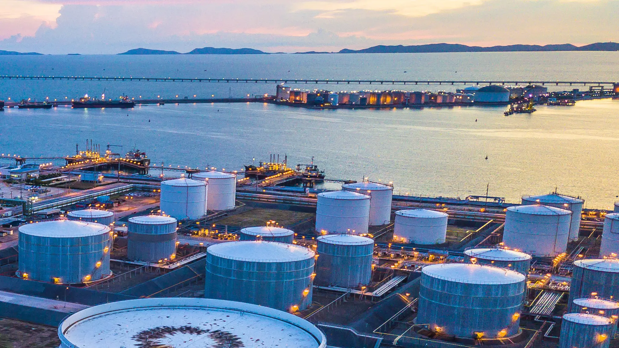 Un complejo industrial petrolero y gasístico con grandes tanques de almacenamiento cerca de un puerto al atardecer